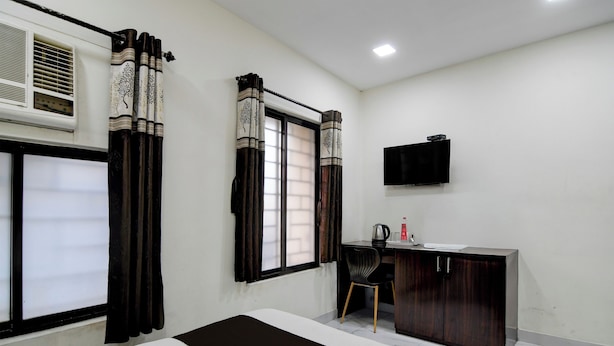 A room with a bed, a desk, a chair, a TV, and a window with curtains.