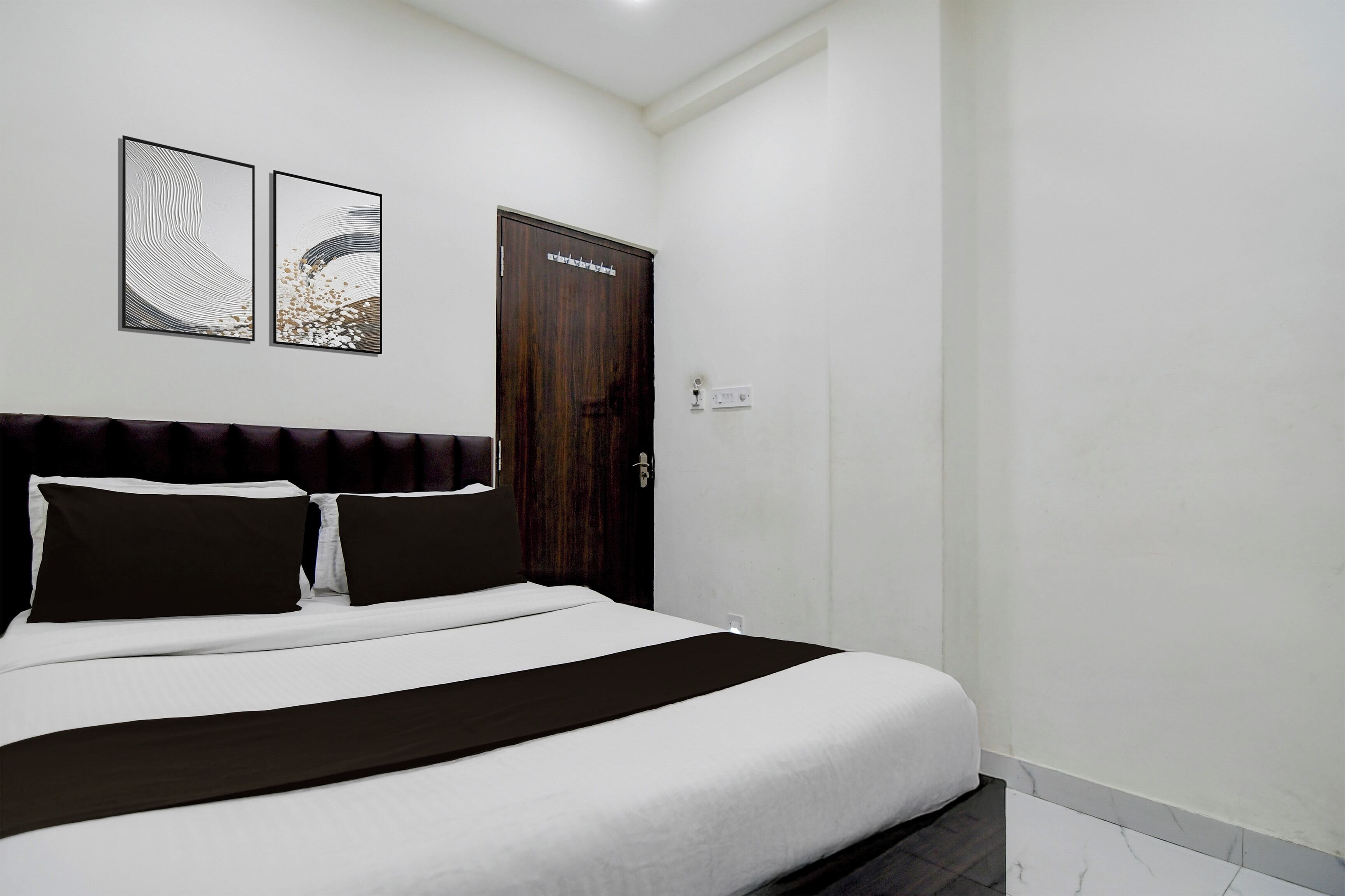 A hotel room with a bed, a dark wooden door, and two abstract paintings on the wall.