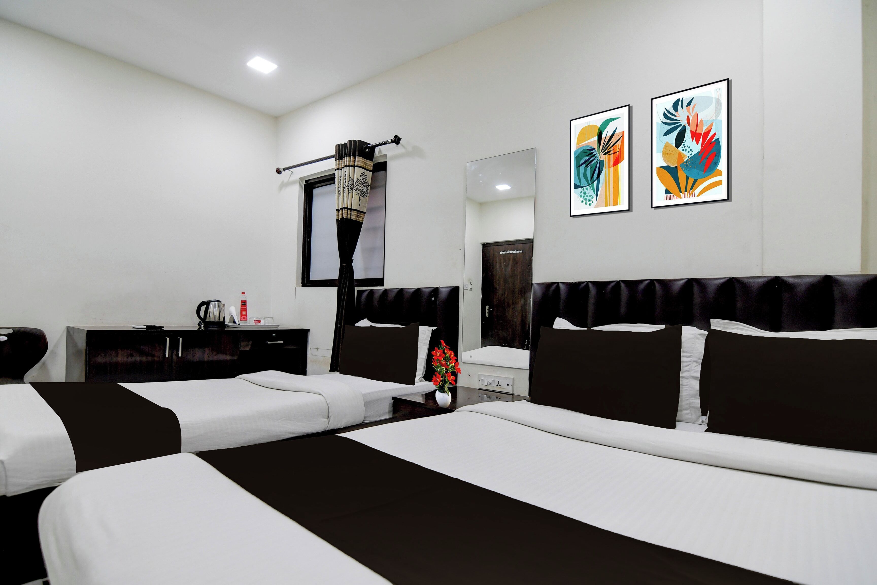 A hotel room with two beds, a desk, a chair, a coffee maker, and two abstract paintings on the wall.