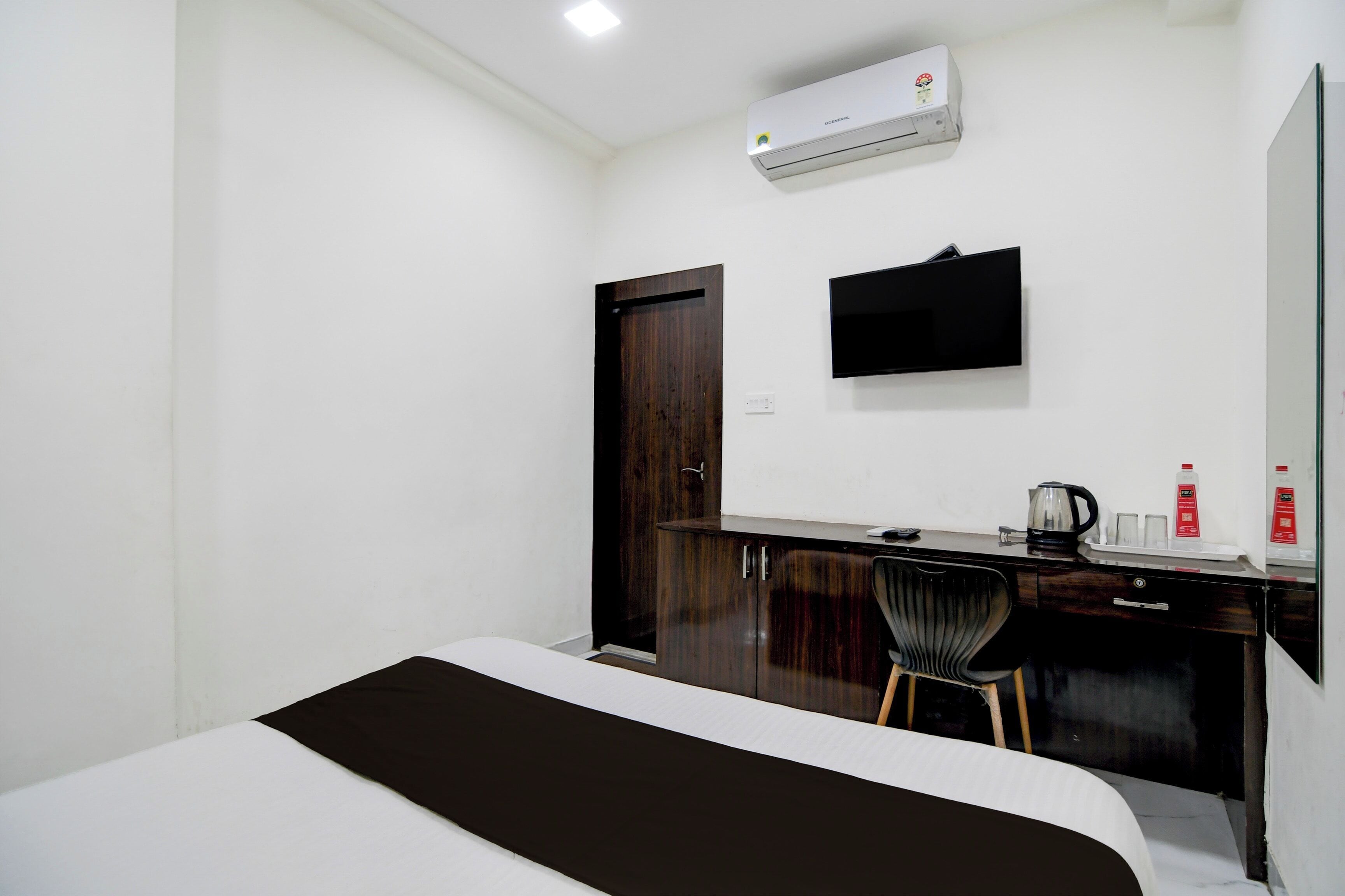 Habitación de hotel con cama, escritorio con silla, televisor de pantalla plana, aire acondicionado y una puerta.