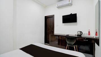 Habitación de hotel con cama, escritorio con silla, televisor de pantalla plana, aire acondicionado y una puerta.