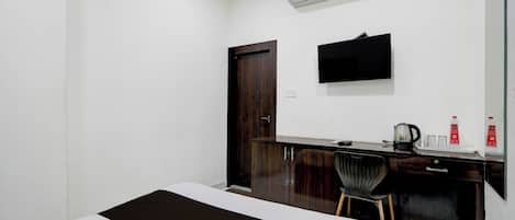A hotel room with a bed, a desk with a chair, a flat-screen TV, an air conditioner, and a door.
