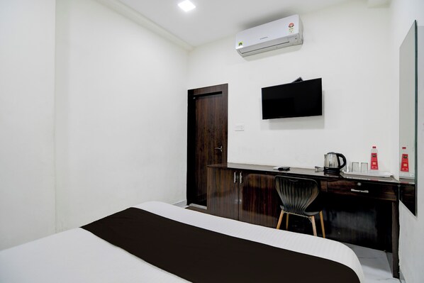 A hotel room with a bed, a desk with a chair, a flat-screen TV, an air conditioner, and a door.