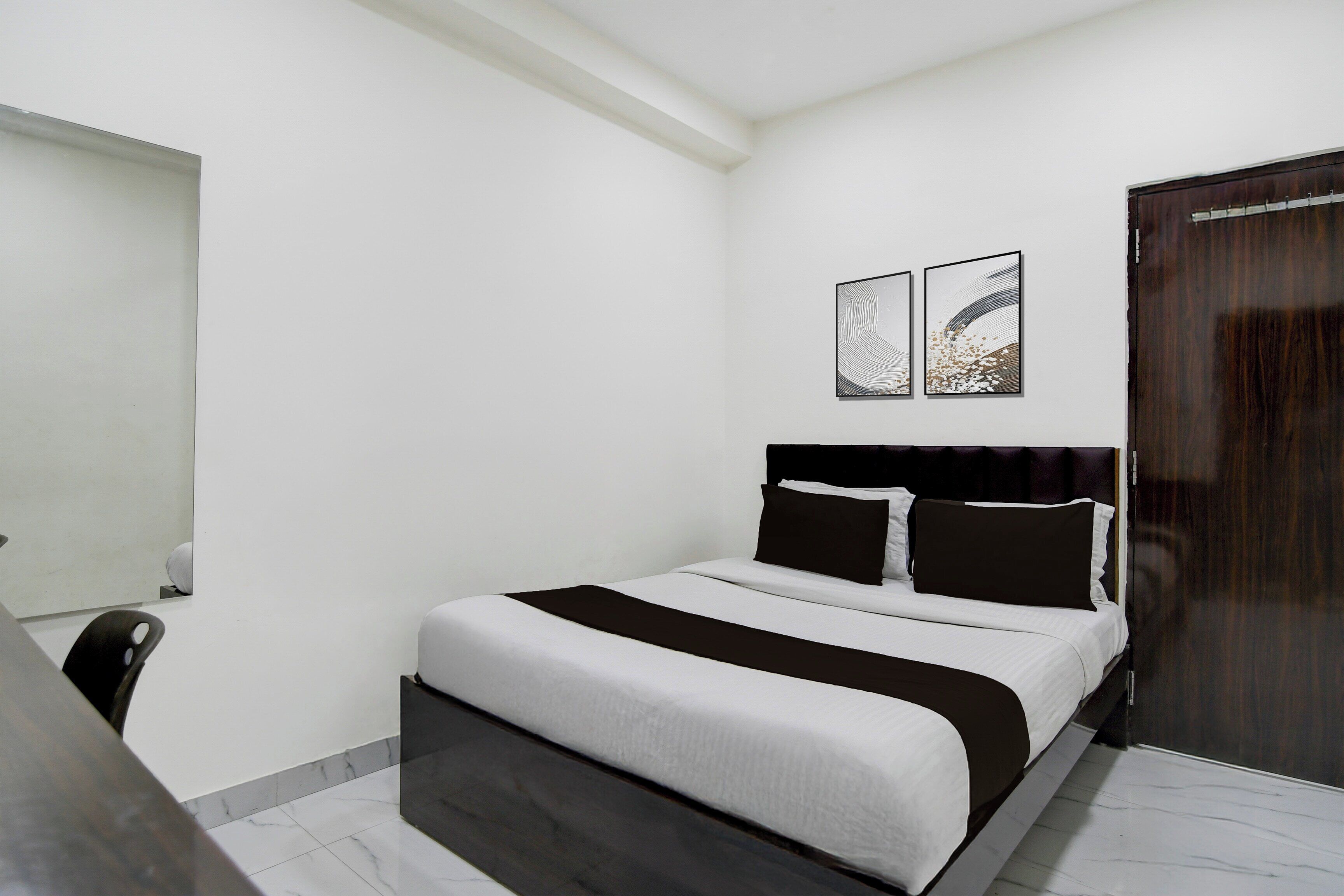 Un dormitorio con cama, mesita de noche, puerta de madera y dos obras de arte colgadas en la pared.