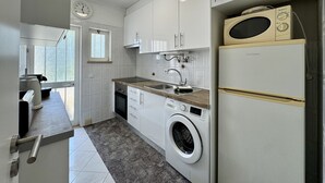 Moderni keittiö, jossa on valkoiset kaapit, sisäänrakennettu pesukone ja mikroaaltouuni.