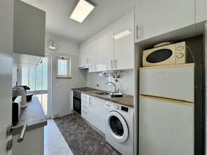 A modern kitchen with white cabinetry, a built-in washing machine, and a microwave. - Vilamoura Golf Apartment 3 by Homing (Loulé)