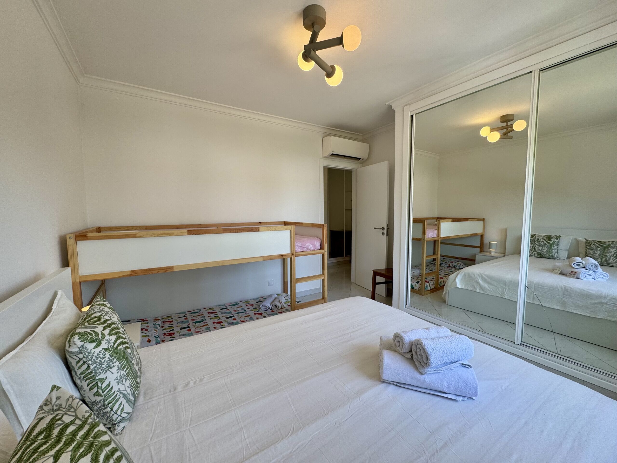 A bedroom with bunk beds, a large mirror, and a ceiling light fixture.