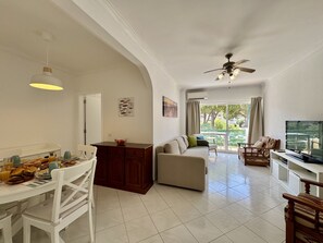 A spacious living area with a dining table set for breakfast, a sofa, and a television. - Vilamoura Golf Apartment 3 by Homing (Loulé)