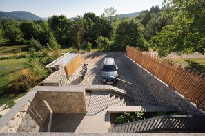 A car parked in a covered parking area with a stone wall and wooden fence.