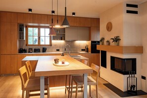 A modern kitchen with wooden cabinets, a central island with seating, pendant lighting, a built-in oven, and a fireplace.
