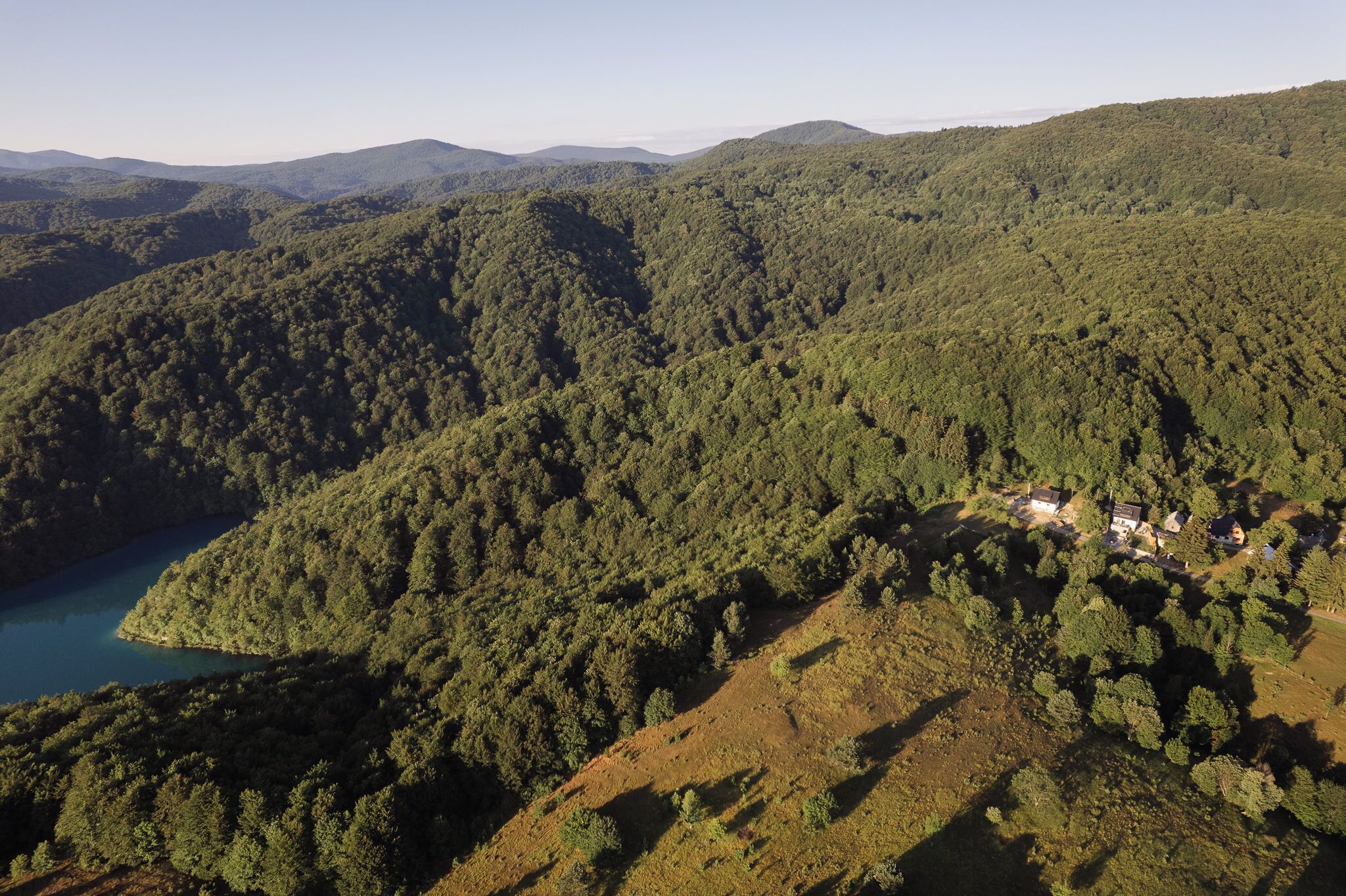 A mountainous landscape with dense forests and a small cluster of buildings near a body of water.