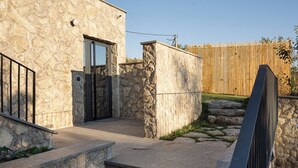 Ein Steinhaus mit einem Metallgitter, Stufen, die zu einer Tür führen, und ein Holzzaun im Hintergrund.