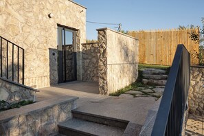 Ein Steinhaus mit einem Metallgitter, Stufen, die zu einer Tür führen, und ein Holzzaun im Hintergrund.