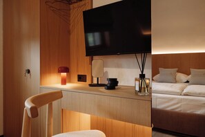 Hotelkamer met een houten bureau, een flatscreen televisie, een lamp, een vaas met een kaars, en een bed met kussens.