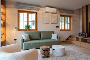 A modern living room with a green sofa, two white poufs, a wooden coffee table, and a staircase.
