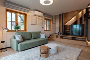 Ein modernes Wohnzimmer mit einem grünen Sofa, einem Flachbildfernseher, Holzlamellen und einem runden Couchtisch.