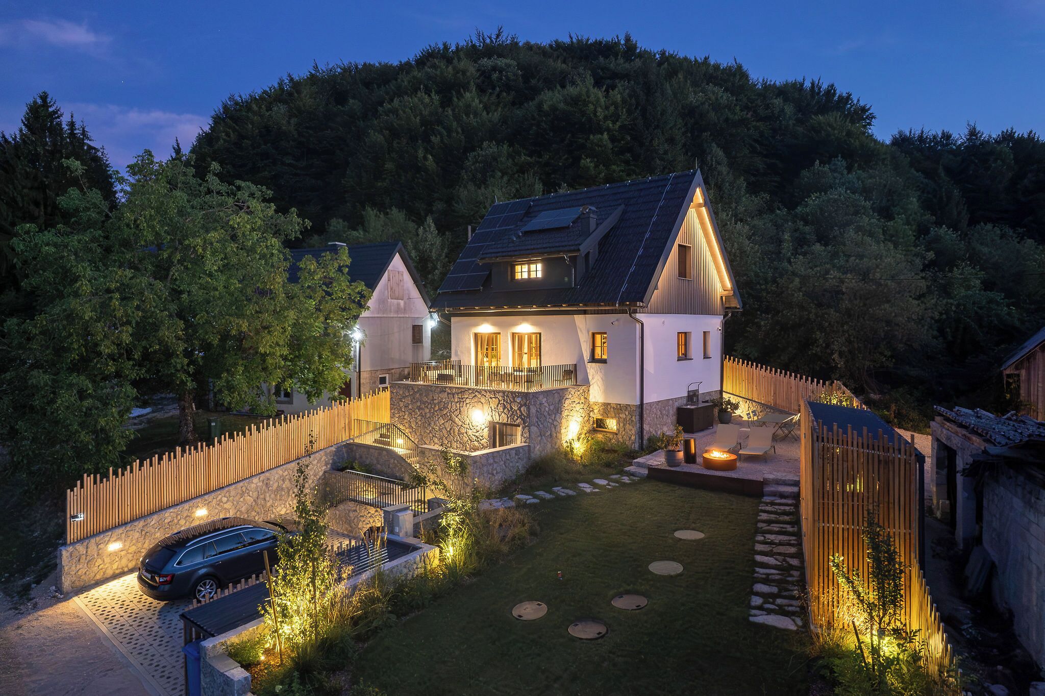 A two-story house with a stone facade, a wooden deck, and a stone pathway leading to the entrance.