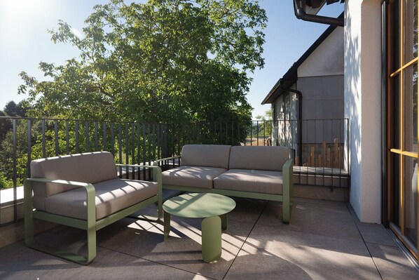 An outdoor seating area with a sofa and chairs, a small table, and a railing.