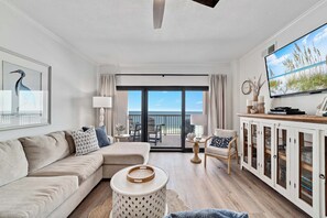 A modern living room with a sofa, a coffee table, a TV, and a view of the ocean. - Gulf front Bliss at The Palms 1015B - Orange Beach, AL - Signature Properties (Orange Beach)
