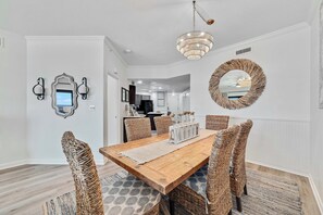 A dining area with a wooden table, woven chairs, and a chandelier. - Gulf front Bliss at The Palms 1015B - Orange Beach, AL - Signature Properties (Orange Beach)