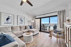 Un salon moderne avec un canapé d’angle, une table basse ronde et une vue sur l’océan grâce à de grandes fenêtres.