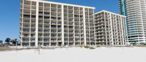 A multi-story hotel with a grid-like facade, located on a sandy beach.