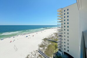 A beach with a pier, a white building with balconies, and a clear blue sky. - Gulf front Bliss at The Palms 1015B - Orange Beach, AL - Signature Properties (Orange Beach)