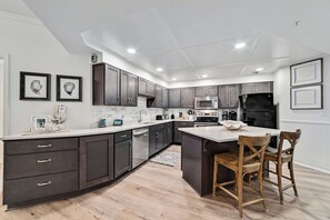A modern kitchen with dark cabinetry, a central island, and a built-in oven. - Gulf front Bliss at The Palms 1015B - Orange Beach, AL - Signature Properties (Orange Beach)