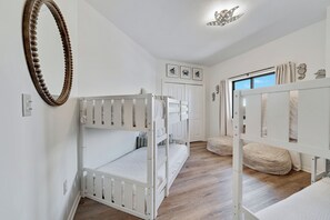 A child's bedroom with bunk beds, a wooden floor, a white door, and a ceiling light fixture. - Gulf front Bliss at The Palms 1015B - Orange Beach, AL - Signature Properties (Orange Beach)