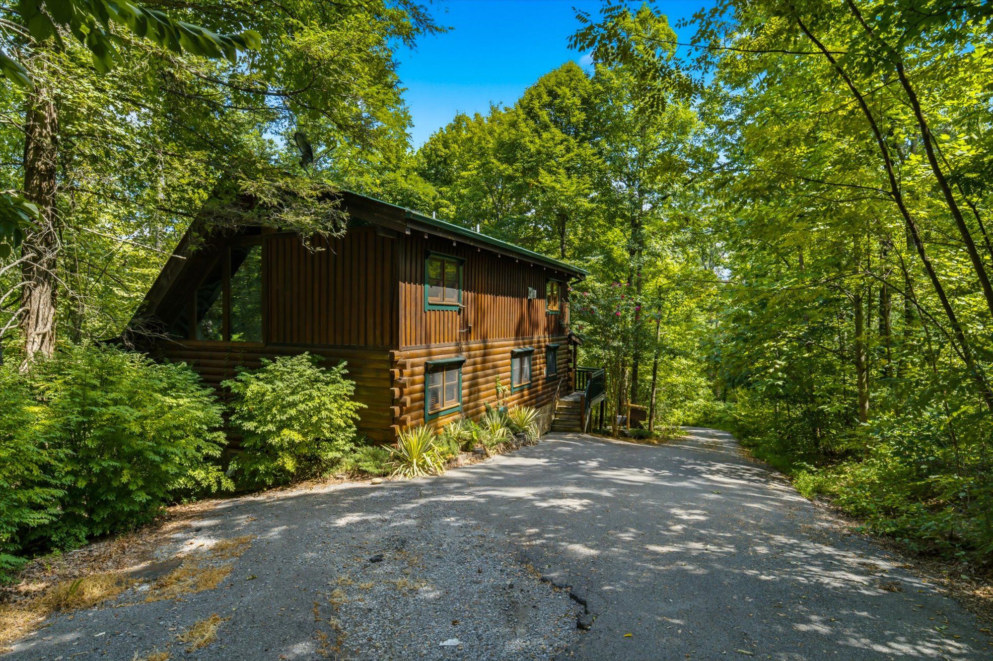 Ein rustikales Blockhaus, umgeben von dichtem Wald, mit einer Schotterauffahrt zum Eingang.