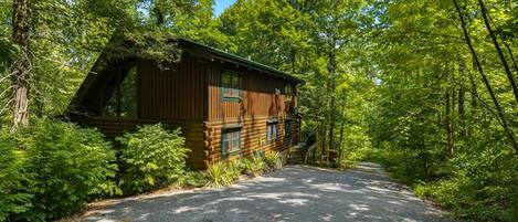 Ein rustikales Blockhaus, umgeben von dichtem Wald, mit einer Schotterauffahrt zum Eingang.