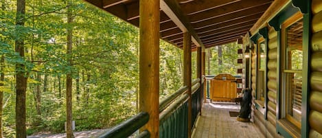 A wooden cabin with a covered porch, surrounded by a forest.