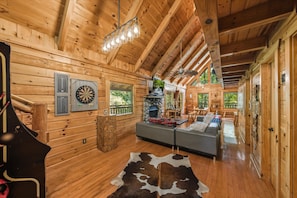 Ein Interieur einer Holzhütte mit Kamin aus Stein, einer Couch, einem Esstisch und einem Cowboysteppich.