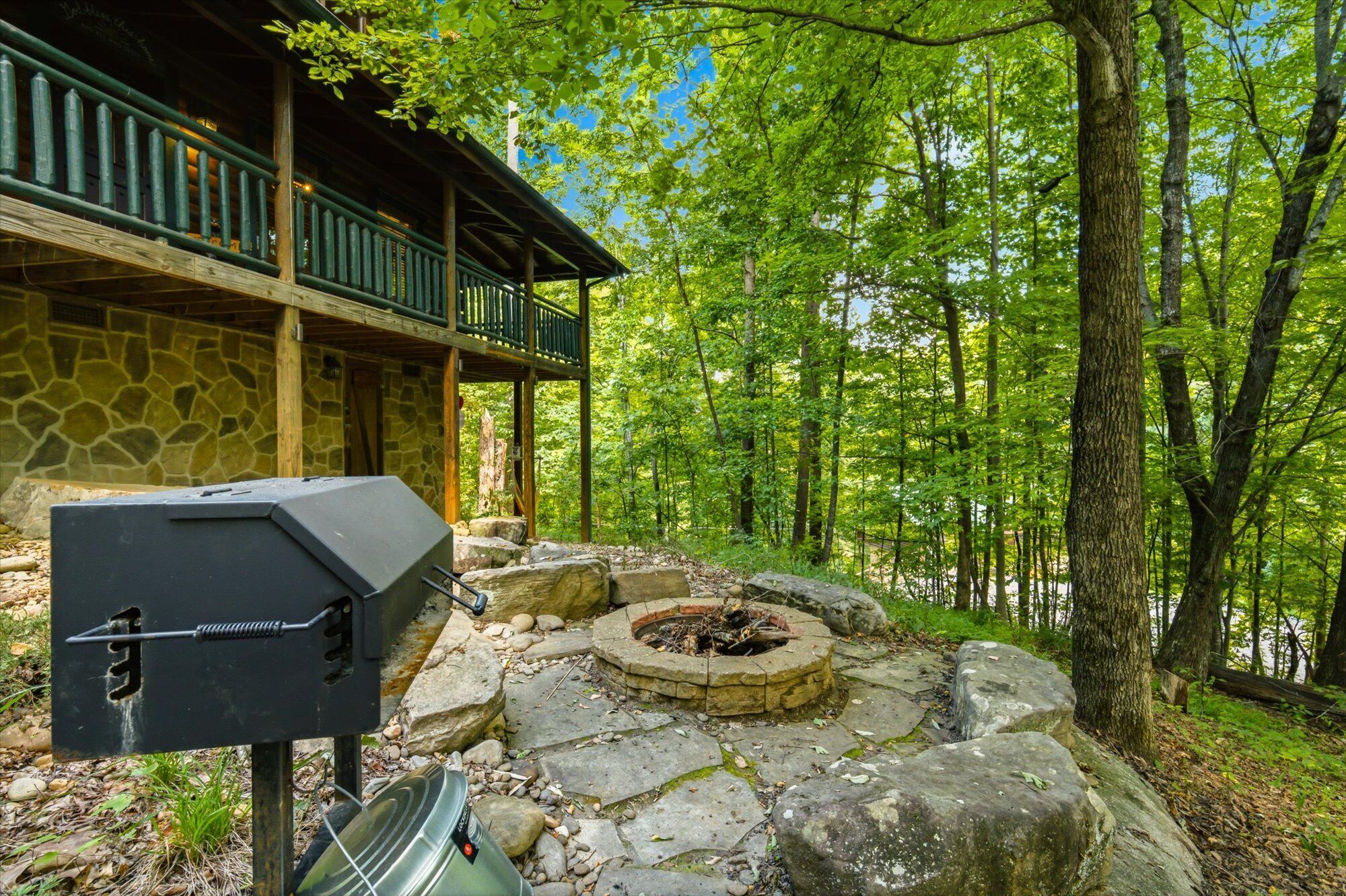 A stone building with a balcony, a grill, and a fire pit in a forest setting.