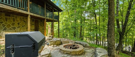 A stone building with a balcony, a grill, and a fire pit in a forest setting.