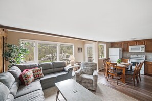 A living room with a grey sofa, a dining table with chairs, and a kitchen area with wooden cabinets and appliances. - Three Bedroom condo- 200 yard walk to ski slopes (Sugar Mountain)