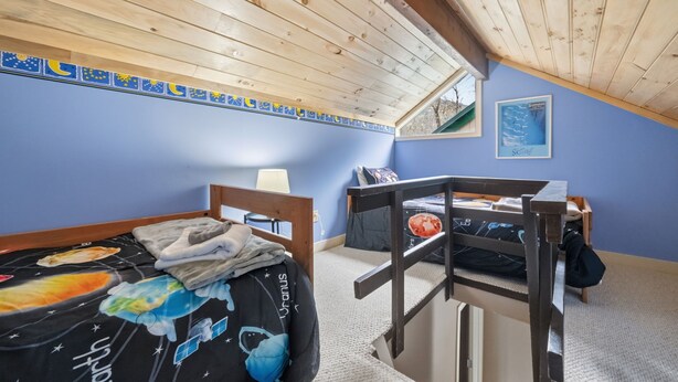 Quarto com teto inclinado, cama beliche, escrivaninha e janela.