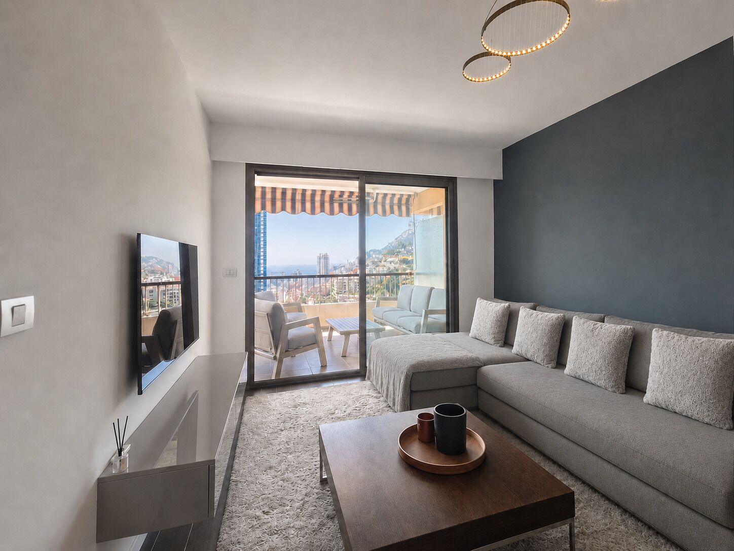 A modern living room with a grey sofa, a coffee table, and a TV mounted on the wall.