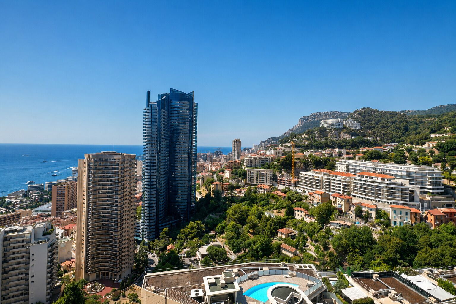 Un paysage urbain côtier avec des immeubles modernes de grande hauteur, un ciel bleu dégagé et une vue sur la mer.
