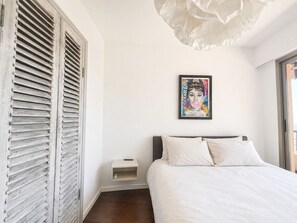 Une chambre à coucher avec un lit, une table de chevet, un tableau encadré au mur et une fenêtre.