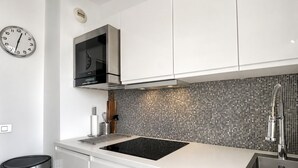 Une cuisine moderne dotée d’une plaque de cuisson à induction noire, d’un évier en acier inoxydable et d’un dosseret carrelé.