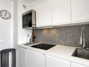 A modern kitchen with a black induction cooktop, stainless steel sink, and a tiled backsplash. - Near Monaco Top Floor Sea View Terrace (Beausoleil)
