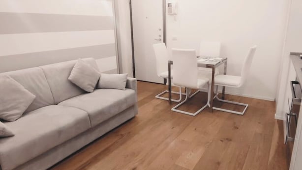 Moderni, pelkistetty olohuone, jossa on sohva, ruokapöytä tuoleineen ja puulattia.