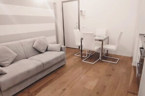 Una sala de estar moderna y minimalista con un sofá, una mesa de comedor con sillas y piso de madera.