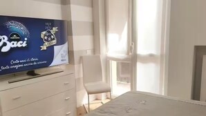 Hotellihuoneessa on lipasto, jonka päällä on litteänäyttöinen televisio, valkoisella peitteellä varustettu sänky, tuoli ja lasiliukuovi, joka johtaa parvekkeelle.