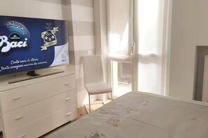 A hotel room with a flat-screen TV on a dresser, a bed with a white bedspread, a chair, and a sliding glass door leading to a balcony. - Duomo & Fashion District -Elegant & Quiet Flat (Milano)