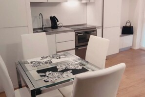 A modern kitchen with white cabinetry, a glass-top dining table, and a black handbag on the wall. - Duomo & Fashion District -Elegant & Quiet Flat (Milano)