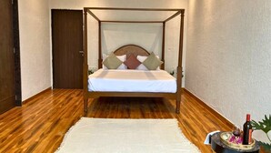 Een hemelbed met houten frame, witte beddengoed en decoratieve kussens.