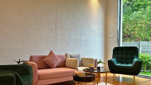 Een moderne woonkamer met een roze bank, een groene fauteuil en een ronde salontafel.