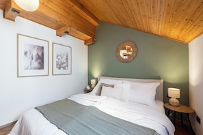A bedroom with a wooden ceiling, a bed with white bedding, two framed pictures on the wall, and a round mirror. - Luxury 2BR Apartment Steps from Old Town Square (Praha)
